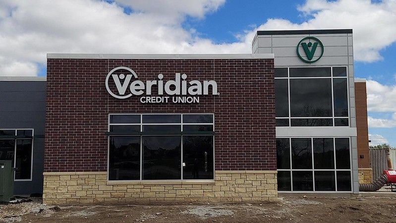 A modern brick and stone Veridian Credit Union branch building under a bright blue sky with clouds.