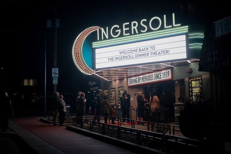A night scene of people entering the illuminated Ingersoll Theater, which has a vintage neon crescent moon sign.