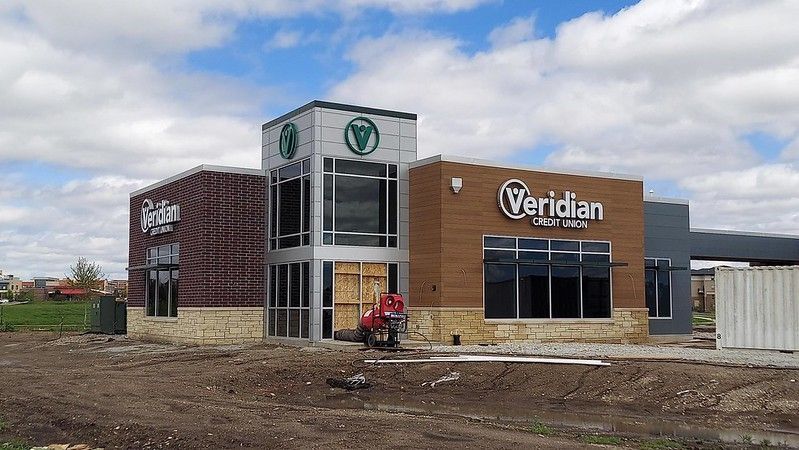 A Veridian Credit Union building under construction with exposed dirt, tan stone, and brown siding on a sunny day.