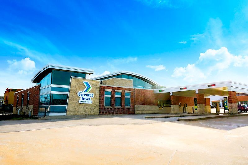 A modern brick and stone building with large glass windows and a drive-thru canopy under a bright blue sky.