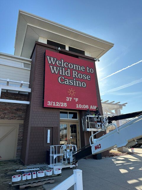 A cherry picker lift is positioned in front of a Wild Rose Casino entrance with a large digital sign showing 37 degrees.