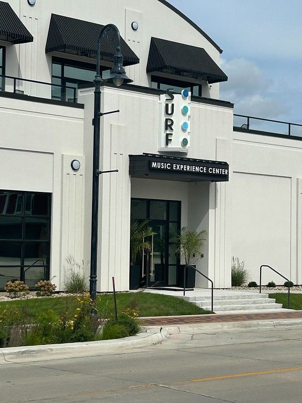 The white Surf Ballroom and Museum exterior entrance with black awnings, a tall lamppost, and steps leading to the door.