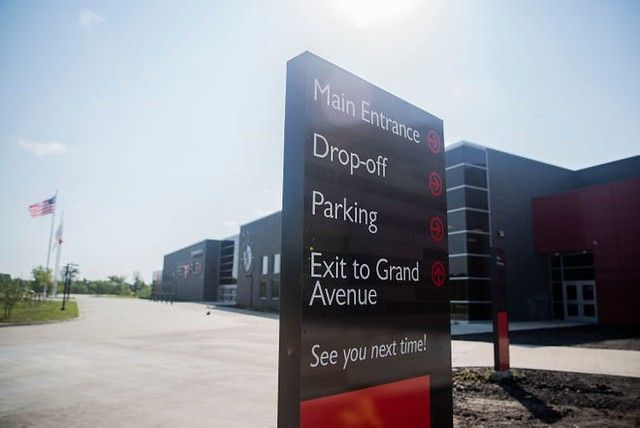 A tall, black directional sign with red accents stands outside a building, listing main entrance, drop-off, and parking.
