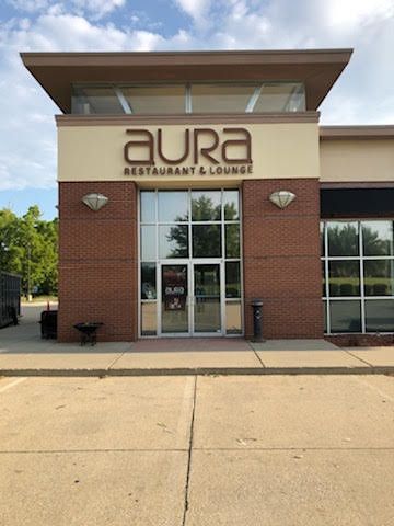 A brick facade of Aura Restaurant & Lounge featuring a central glass entrance and dark, modern signage under a canopy.