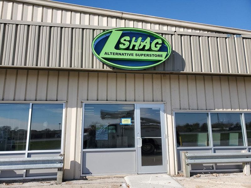 Exterior view of the Shag Alternative Superstore, a one-story tan building with large glass windows and a green oval sign.
