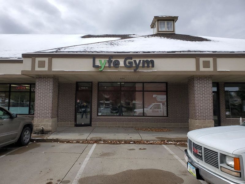 A storefront for Lyte Gym, featuring tan brick pillars, a snow-covered roof, and parking spaces in front.
