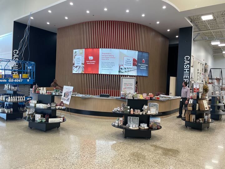 Service desk in a bright retail store with a curved wooden wall, digital signage, and cashier stations on either side.