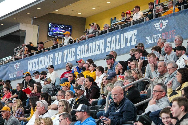 A crowd of spectators watches an event under a large blue banner that reads 