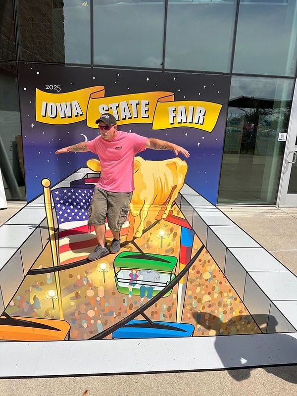 A person in a pink shirt balances on a 3D floor mural depicting a tightrope at the Iowa State Fair.
