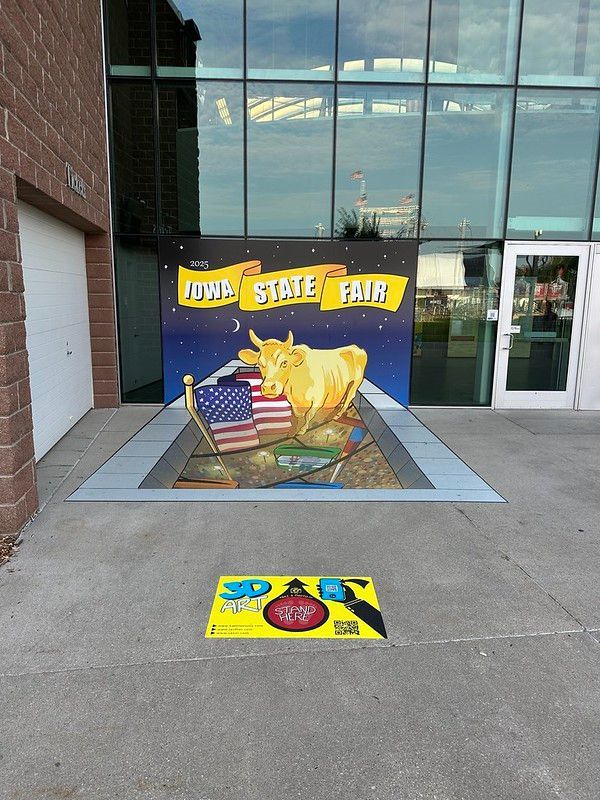 A 3D street painting of a golden cow and US flag at the Iowa State Fair, with a ground marker showing where to stand.