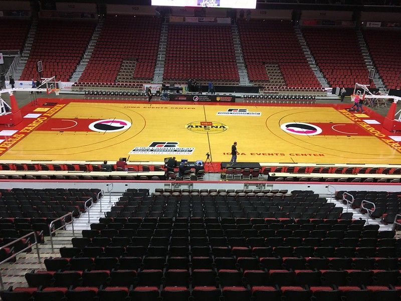 Empty yellow basketball court inside a large arena with red stadium seating.