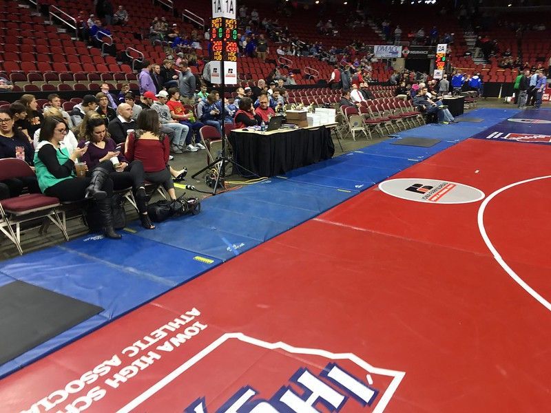 Spectators watch a wrestling match at an Iowa High School Athletic Association event on a red and blue floor mat.