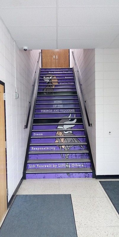 Stairs painted purple with the Vikings logo and white text leading up to a wooden door in a school hallway.