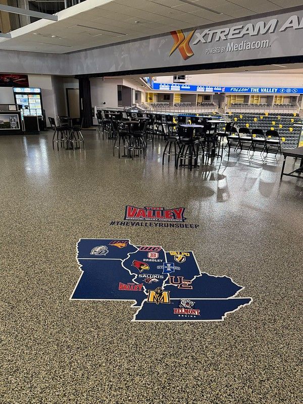 Floor graphic of an Iowa map featuring collegiate logos inside a seating area overlooking the Xtream Arena.