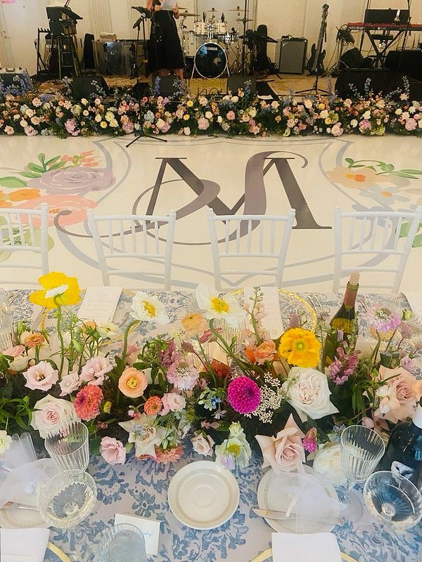 A floral arrangement centers a table set for a wedding reception in front of a dance floor with a monogrammed centerpiece.