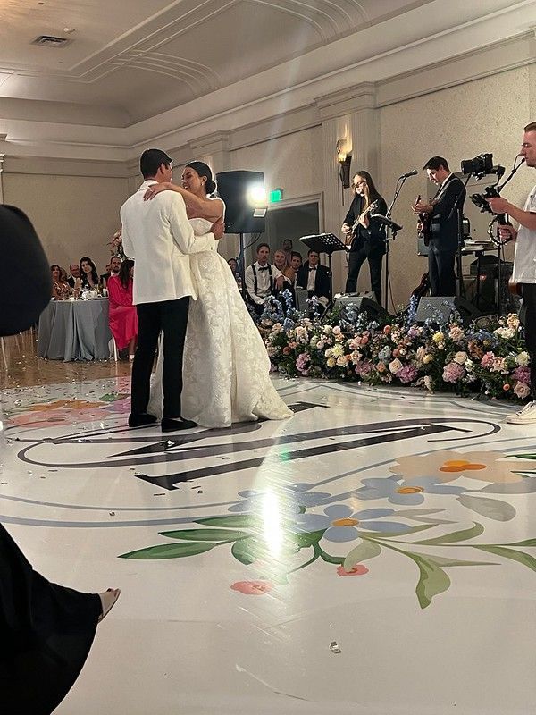 A bride and groom share their first dance on a custom dance floor as a band plays in the background at a wedding reception.