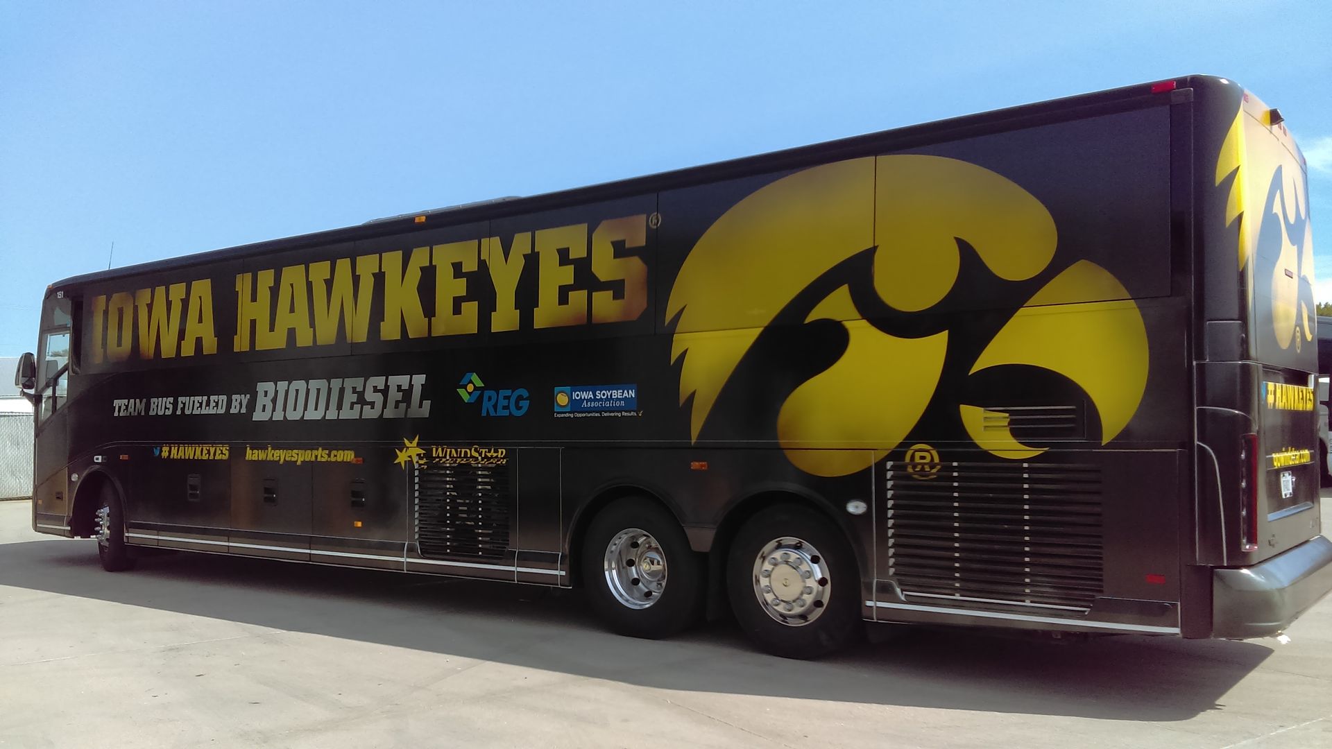 Iowa Hawkeyes team bus with large black and gold logo parked outdoors.