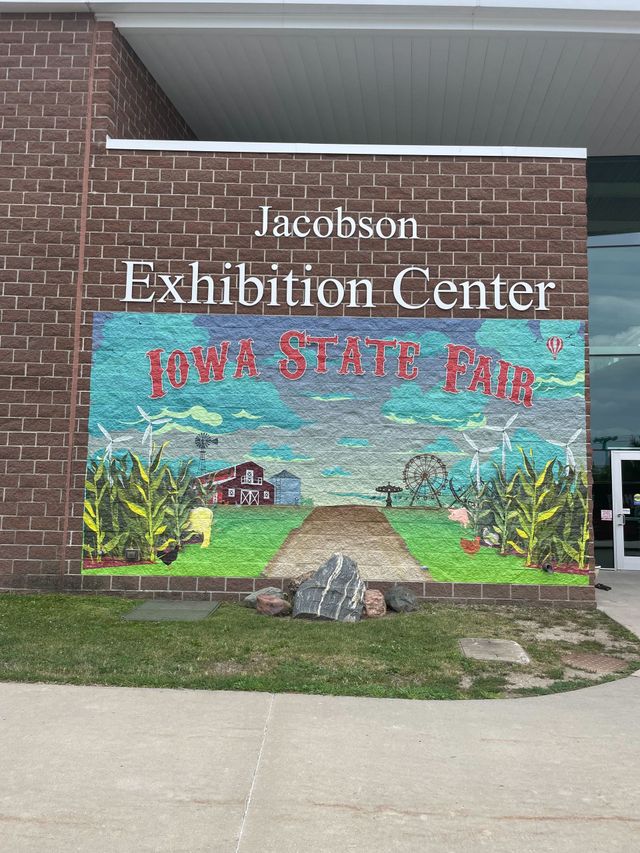 Mosaic mural at Jacobson Exhibition Center reading Iowa State Fair, beside a brick building.