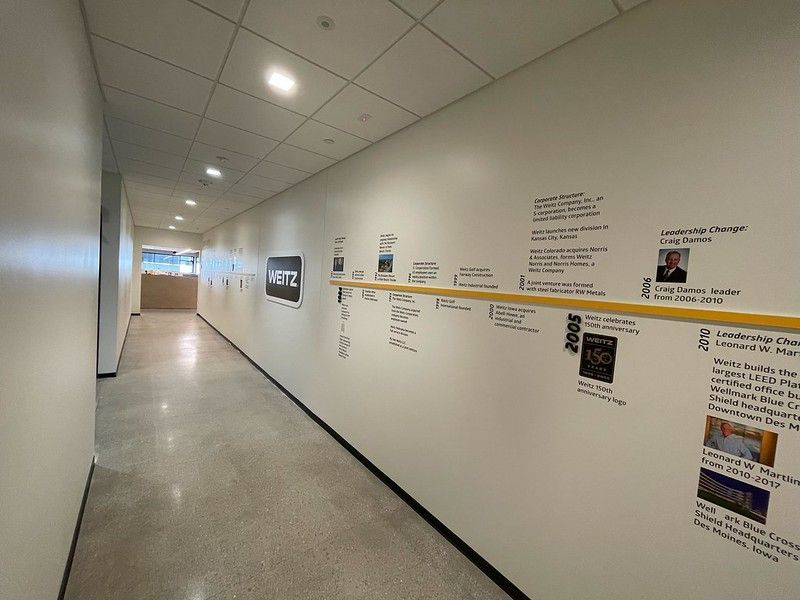 A hallway with a company history timeline on the wall featuring photos, text, and dates along a yellow horizontal line.
