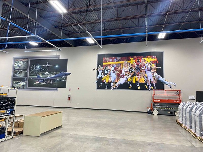 A large industrial space with a ceiling featuring exposed trusses and two wall murals: one of an aircraft, one of football.