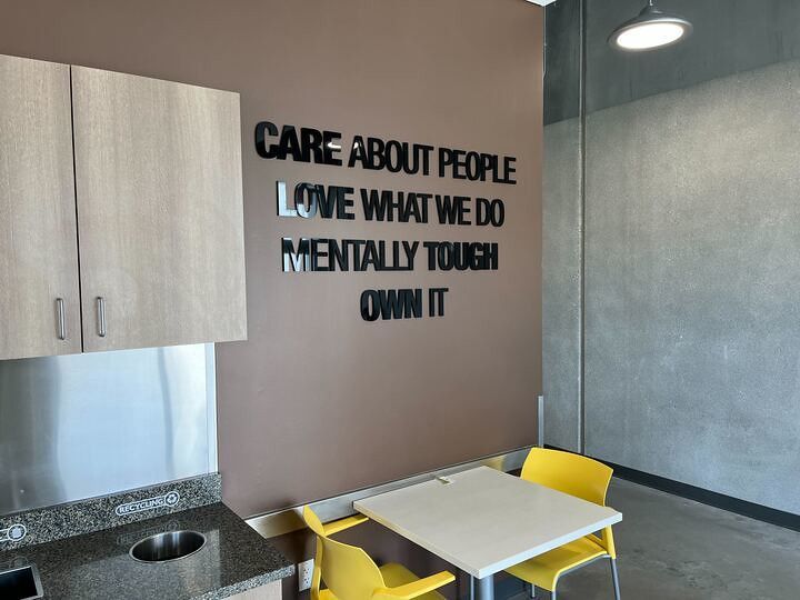 A brown wall featuring black lettering with the text: CARE ABOUT PEOPLE, LOVE WHAT WE DO, MENTALLY TOUGH, OWN IT.