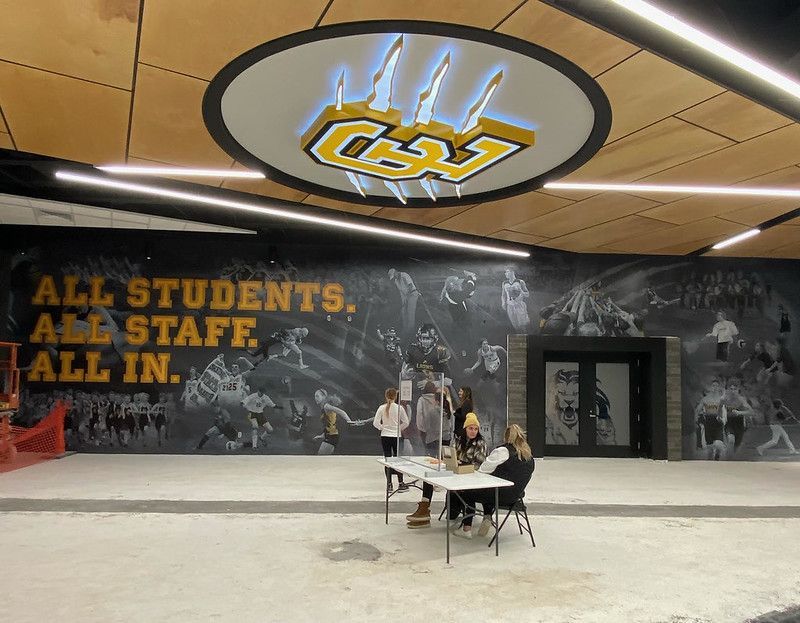 People sit at a table in a modern hall with a mural reading 
