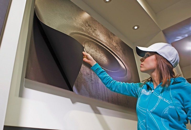 A person in a blue hoodie and white cap peels a layer off a large circular wall graphic.