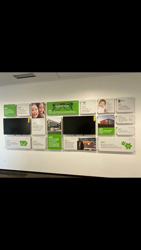 A wall display in an office with screens, branded green signage, photos, and informational placards.