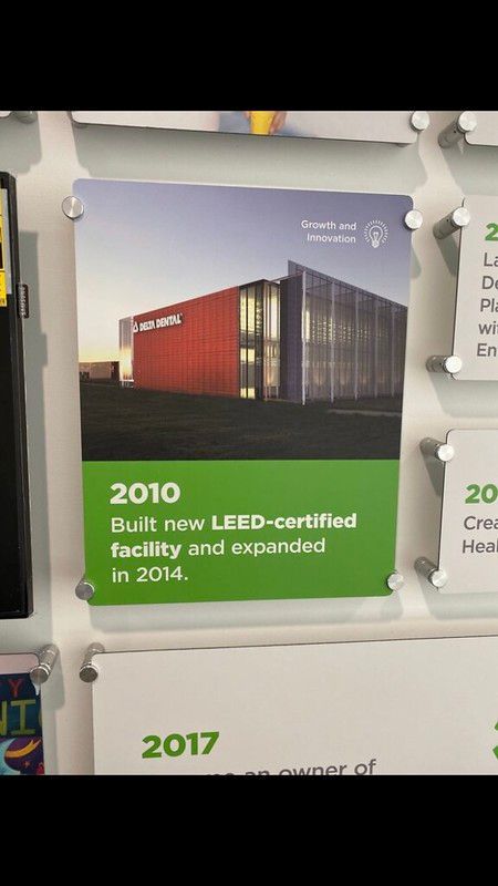 A plaque on a wall displays a photo of a red and metal building with text noting a 2010 LEED-certified facility expansion.