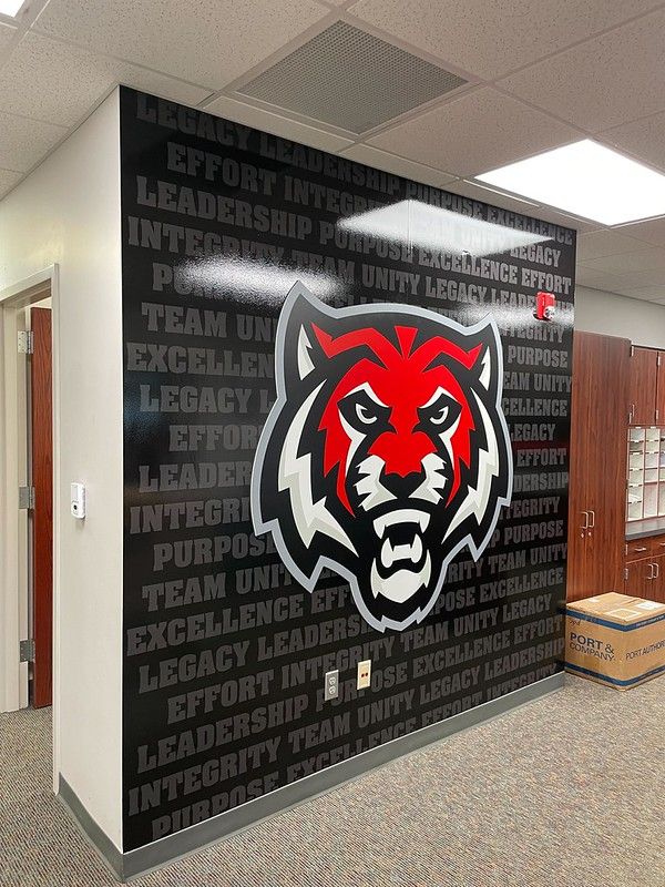 A school wall mural features a large red and white tiger mascot over a dark background with repeated motivational words.