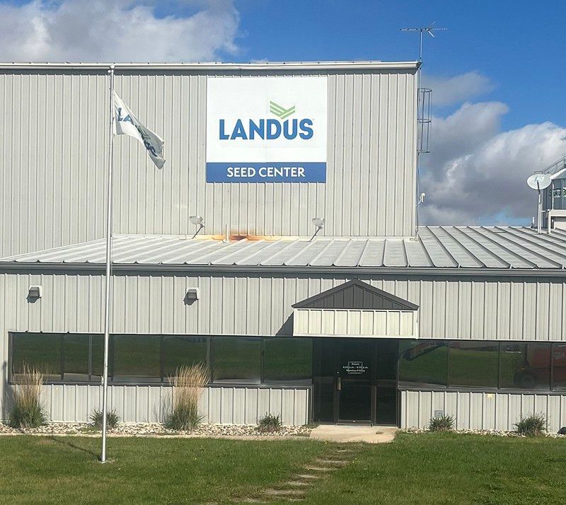 A Landus Seed Center sign on the side of a metal industrial building under a blue sky with clouds.