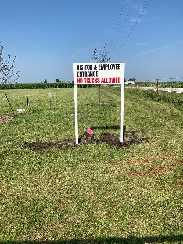 A white sign on two posts in a grassy field reads 