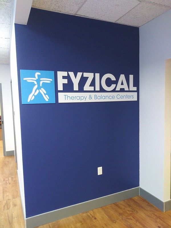 A blue wall features the Fyzical Therapy & Balance Centers logo, a white stylized human figure in a blue square.