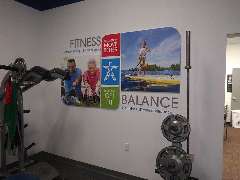 Wall graphic in a gym featuring paddleboarding and workout imagery with text promoting fitness and balance.