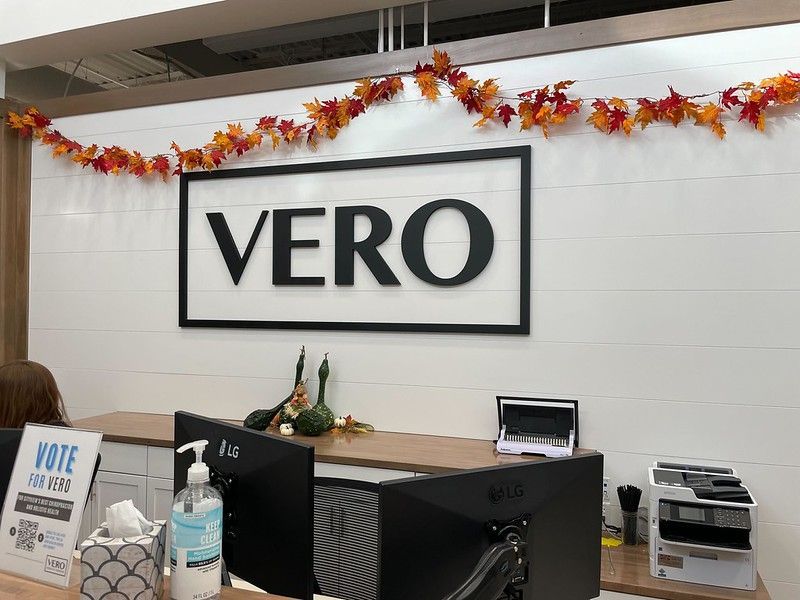 A reception desk with a VERO sign, decorated with autumn leaves and decor, in a brightly lit office setting.