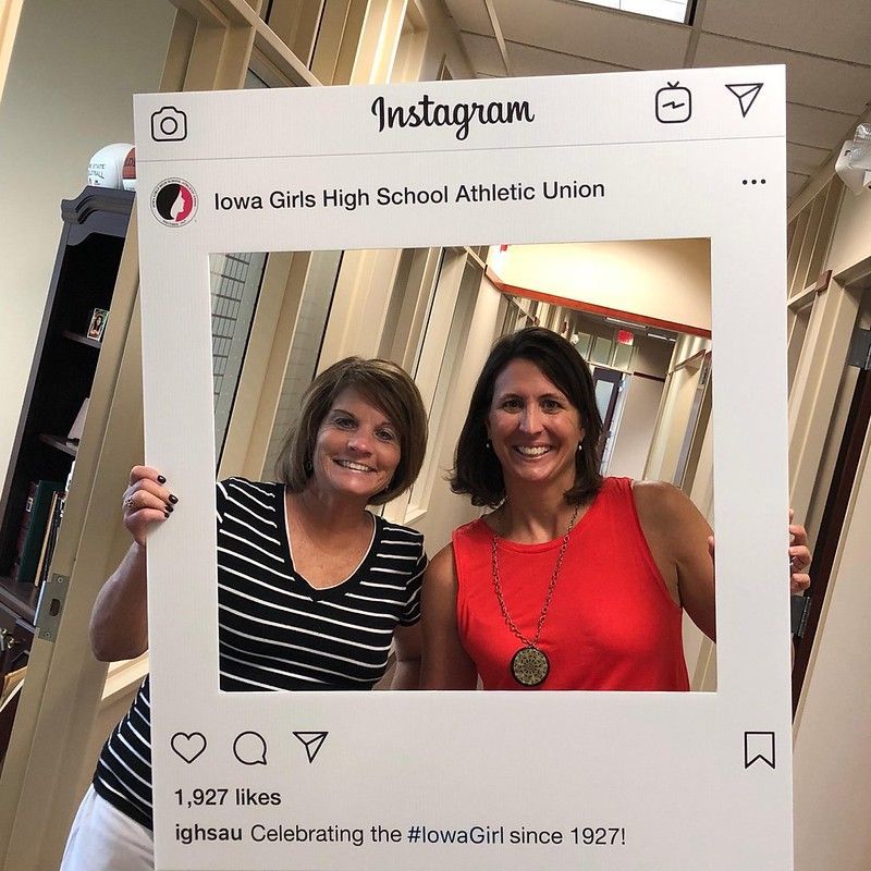 Two smiling women hold an Instagram-style cutout frame featuring the logo and text of the Iowa Girls High School Athletic Union.