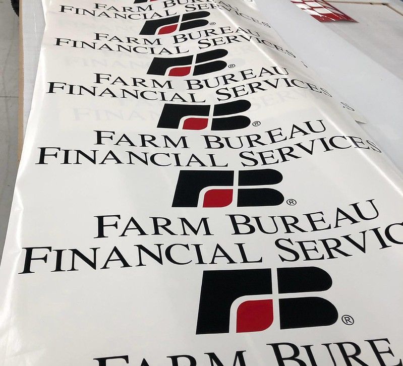 A roll of vinyl signage featuring the Farm Bureau Financial Services logo in black and red text on a white background.