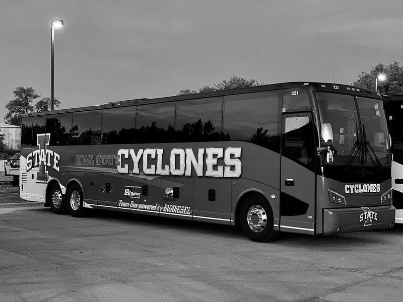 A black and white photo of an Iowa State Cyclones branded tour bus parked in a lot under streetlights.