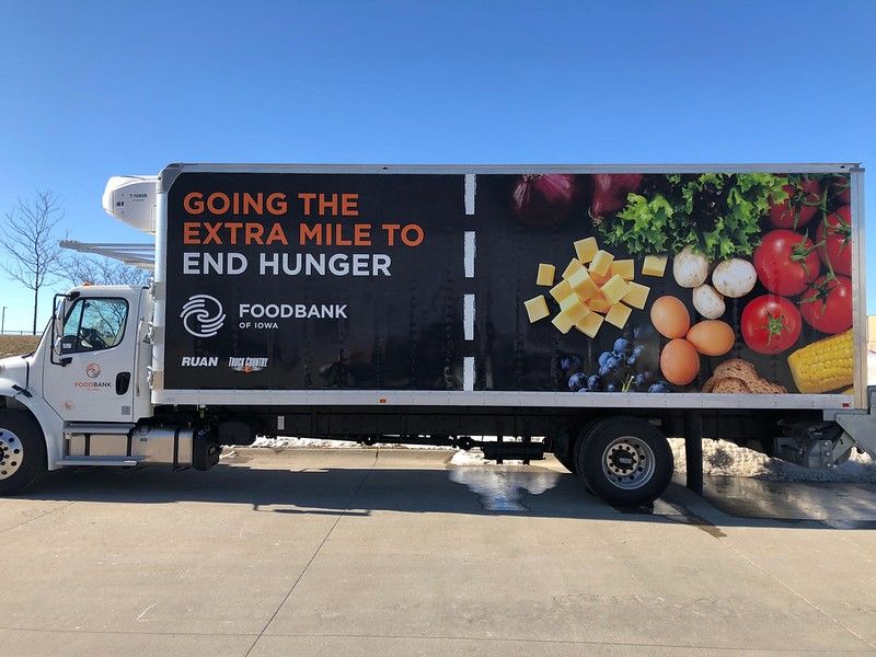 A white Foodbank of Iowa delivery truck parked on a sunny day, featuring a graphic of fresh produce and 