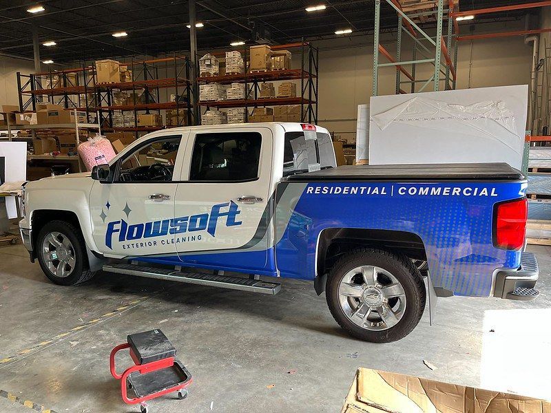 A white and blue branded Flowsoft pickup truck parked inside a warehouse with industrial shelving in the background.