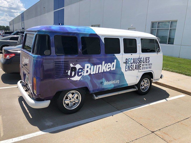 A parked Volkswagen bus wrapped in blue and white, featuring the text 