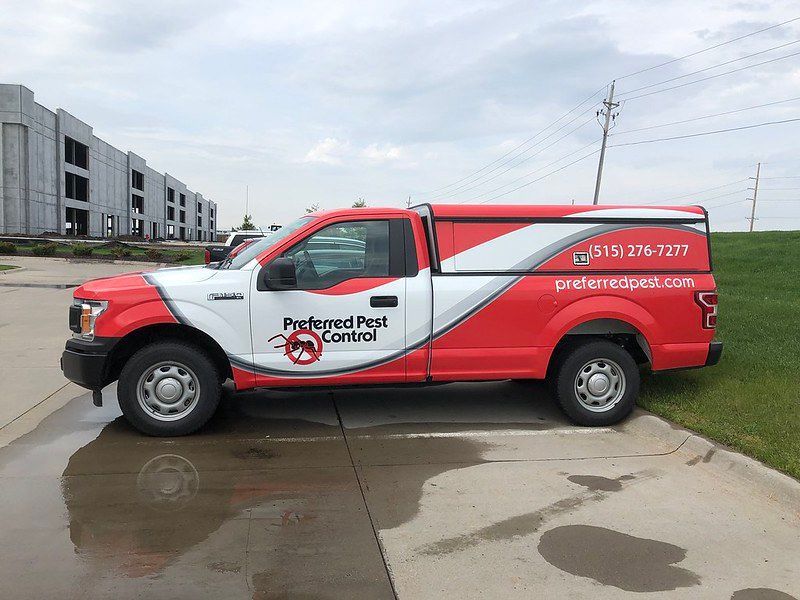A red and white Preferred Pest Control truck parked on a concrete lot near a construction site.