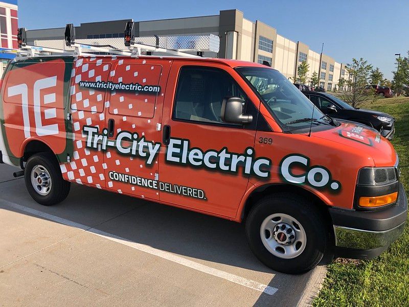 A bright orange Tri-City Electric Co. work van parked in a lot during the day.