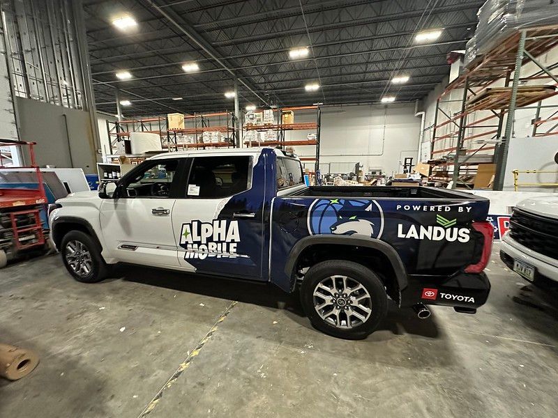 A white and blue branded Toyota pickup truck parked inside a large warehouse with industrial shelving in the background.
