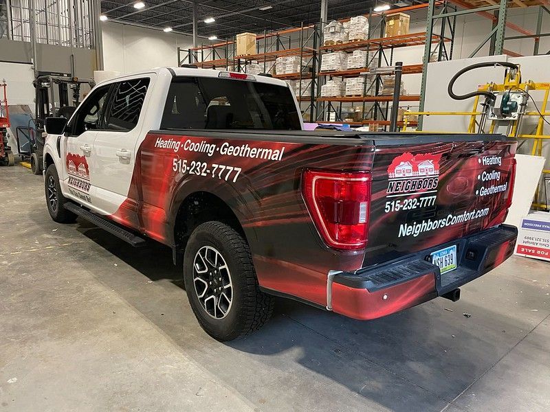 White pickup truck with a branded red and black graphic wrap parked in a warehouse.