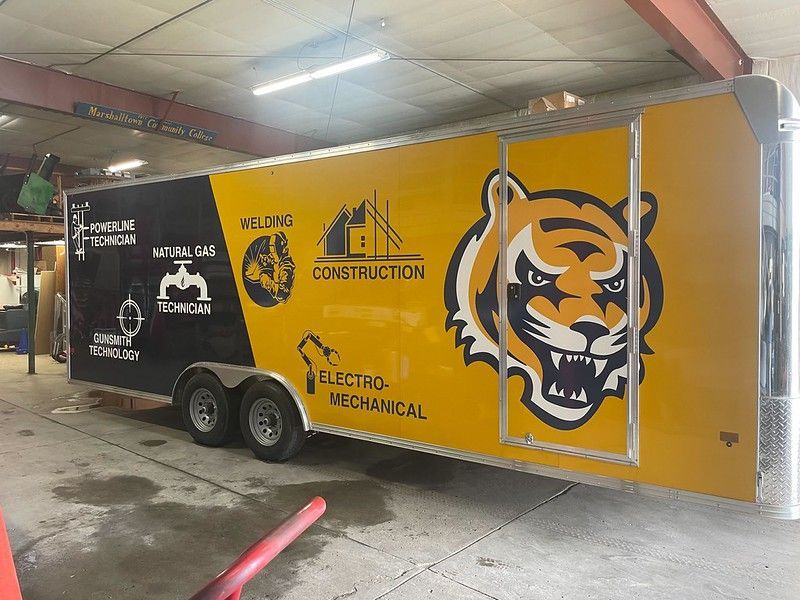 A yellow and black trailer featuring a tiger mascot graphic and icons for construction, gas, and electrical services.