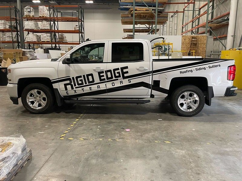 A white pickup truck with black Rigid Edge Exteriors decals, parked inside a warehouse storage facility.