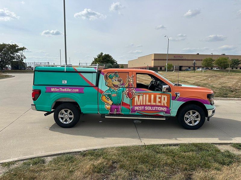 A teal and orange work truck parked on concrete with a cartoon mascot graphic and the text 