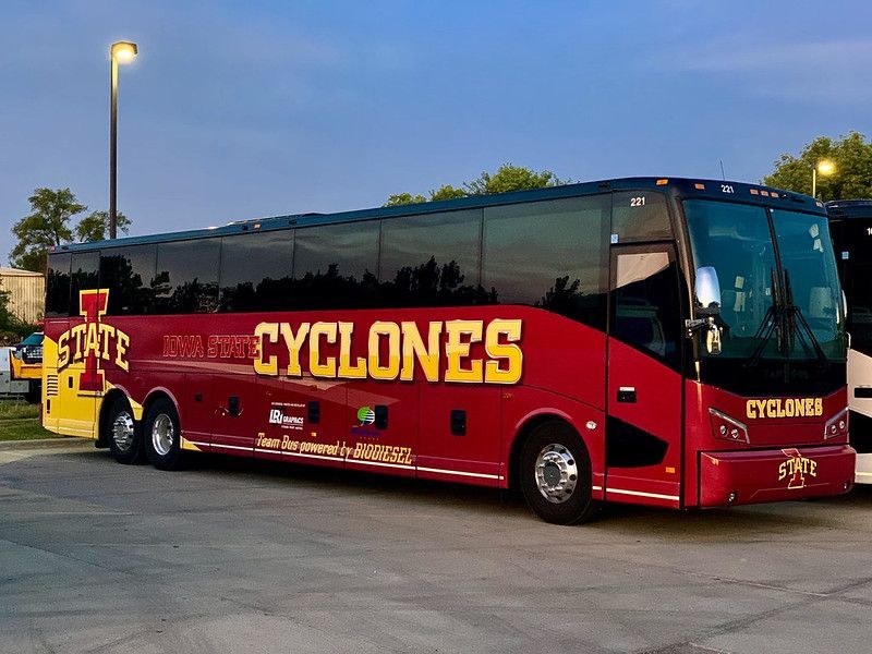 A red Iowa State University Cyclones charter bus parked outdoors during the evening.