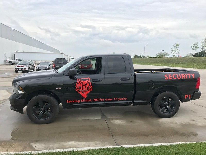 Black Dodge Ram security truck parked outside a warehouse on a cloudy day, featuring red branding on the side.